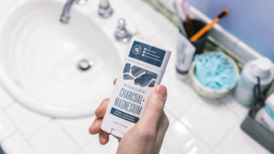 man holding charcoal magnesium deodorant by schmidt's on bathroom sink